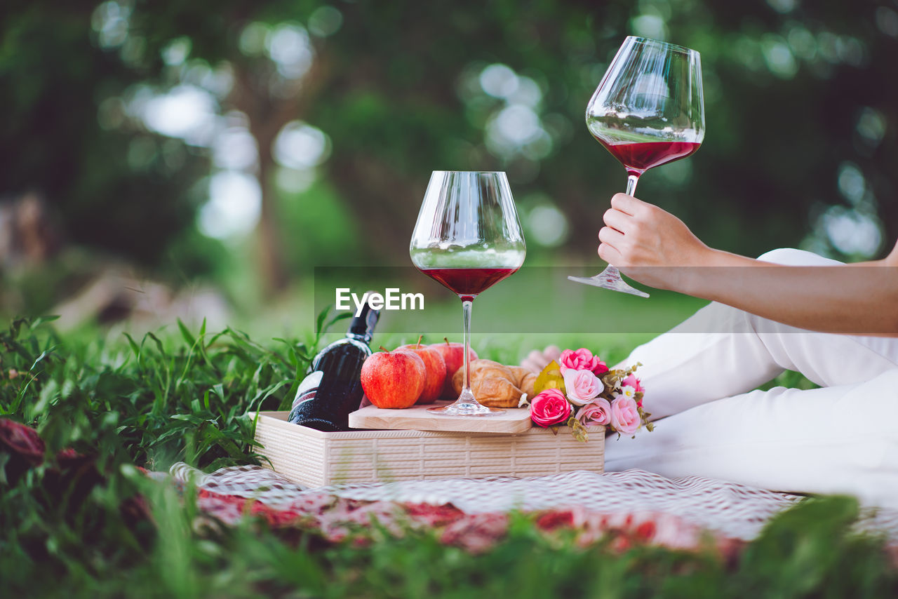 Midsection of woman having wine while sitting on field at park