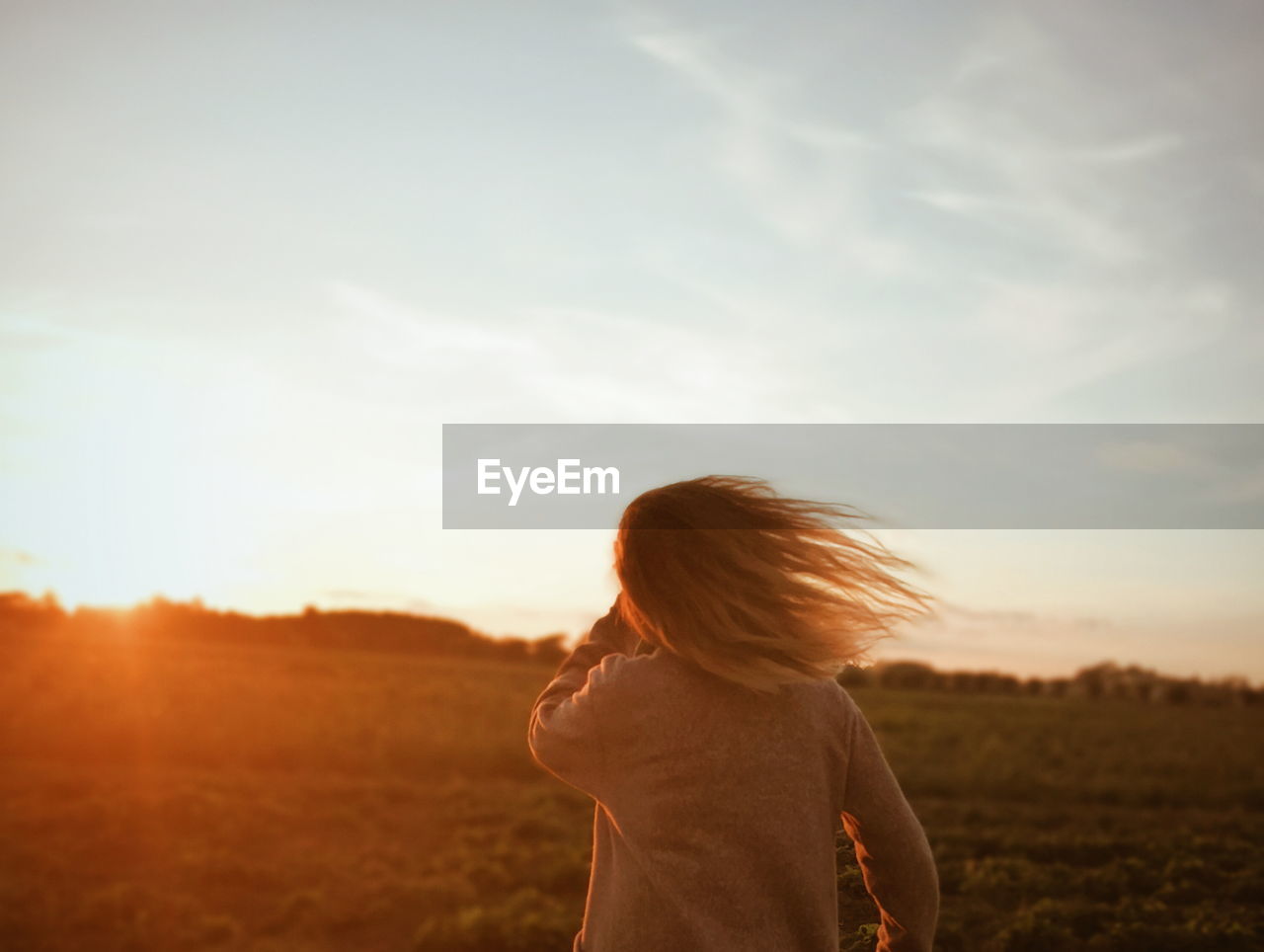 Rear view of girl standing on field during sunset