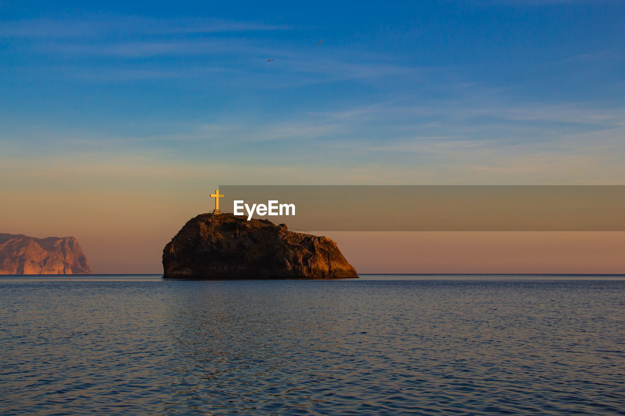 Rock formation in sea against sky during sunset