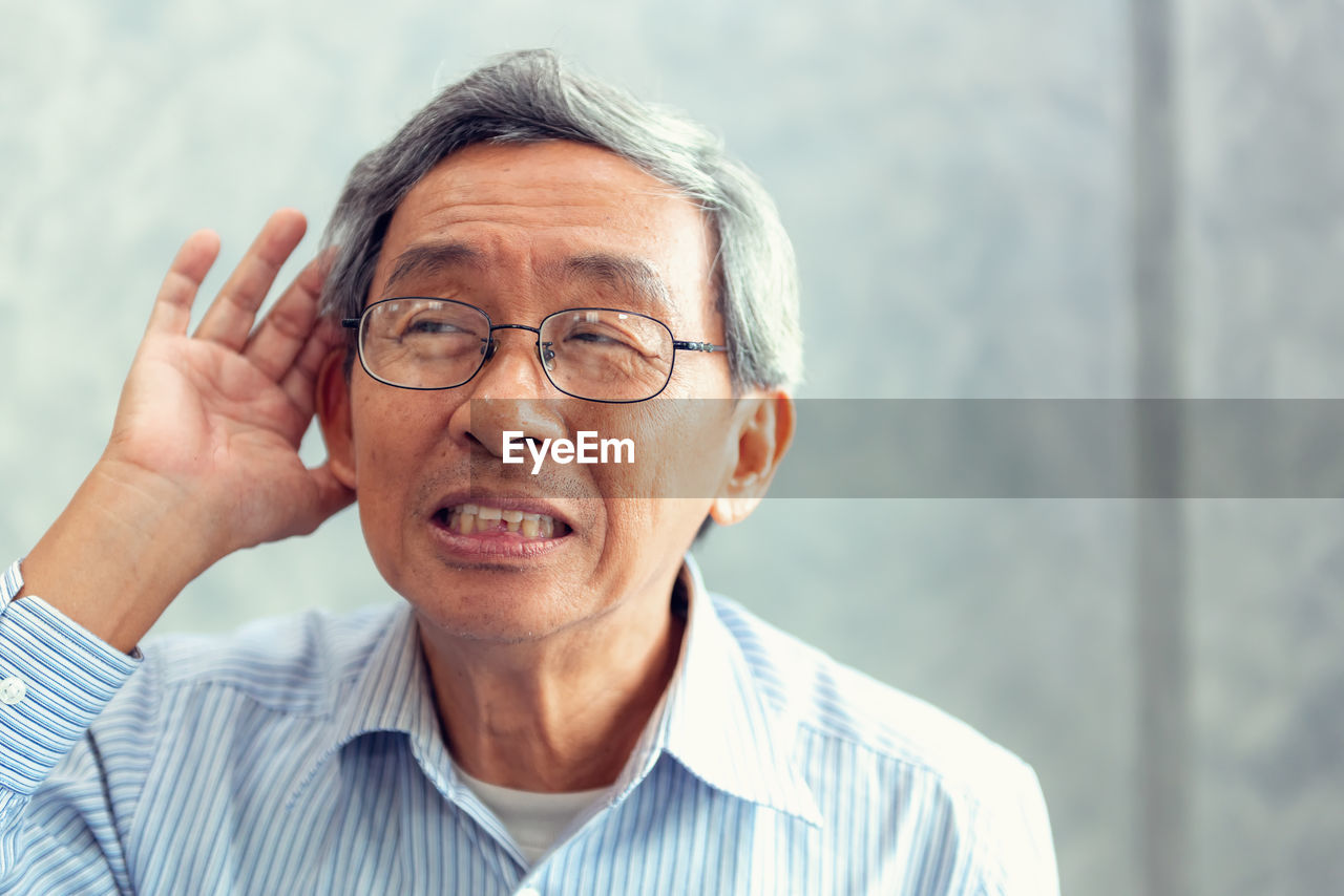 Close-up of man wearing eyeglasses listening while standing against wall