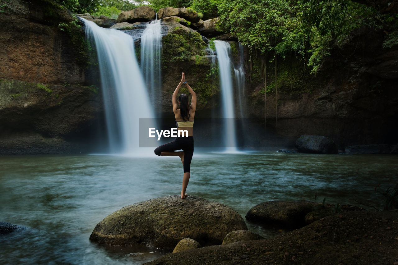 Rear view of woman practicing yoga by waterfall in forest