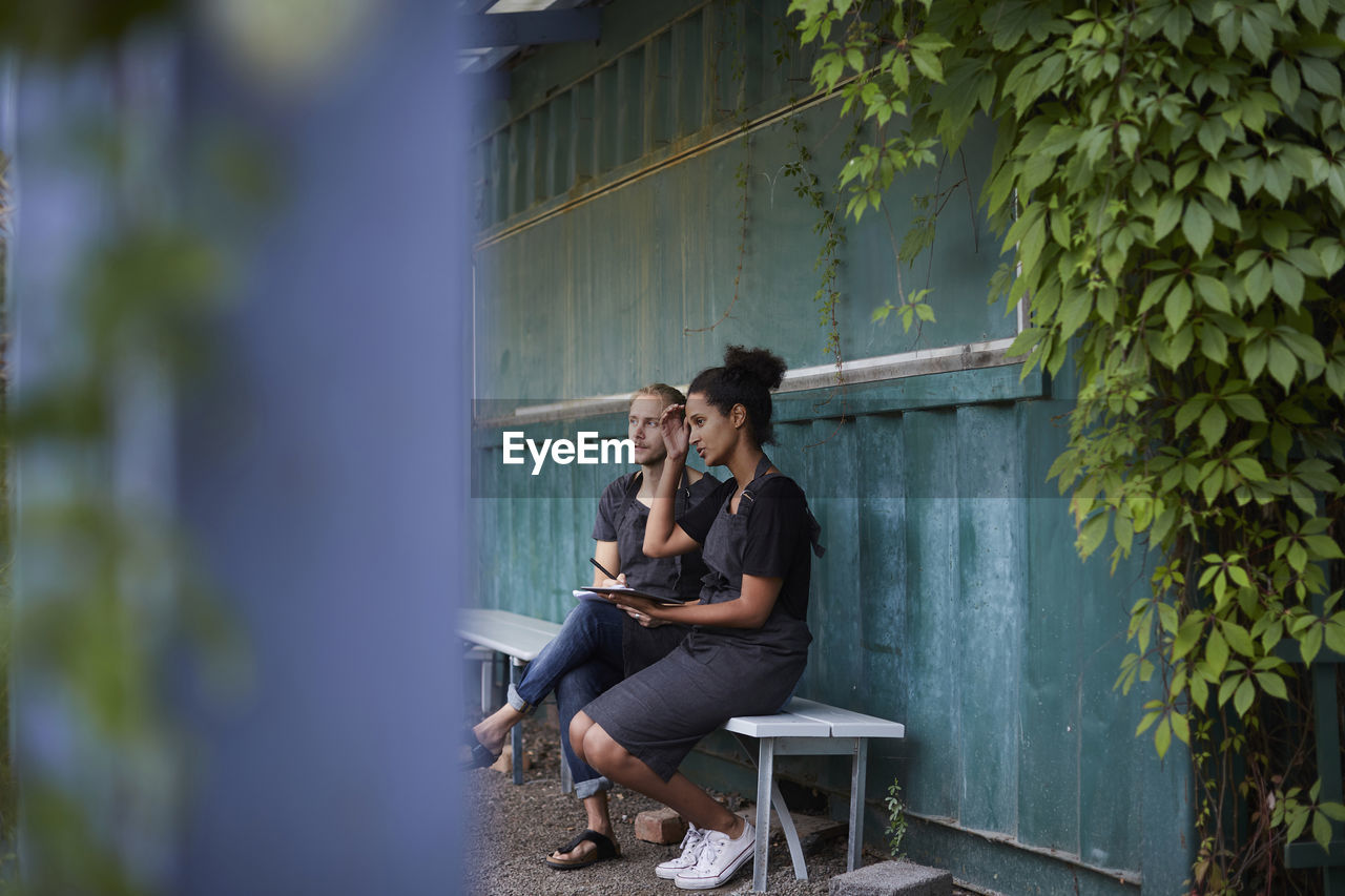 Gardeners looking away while sitting on bench at yard