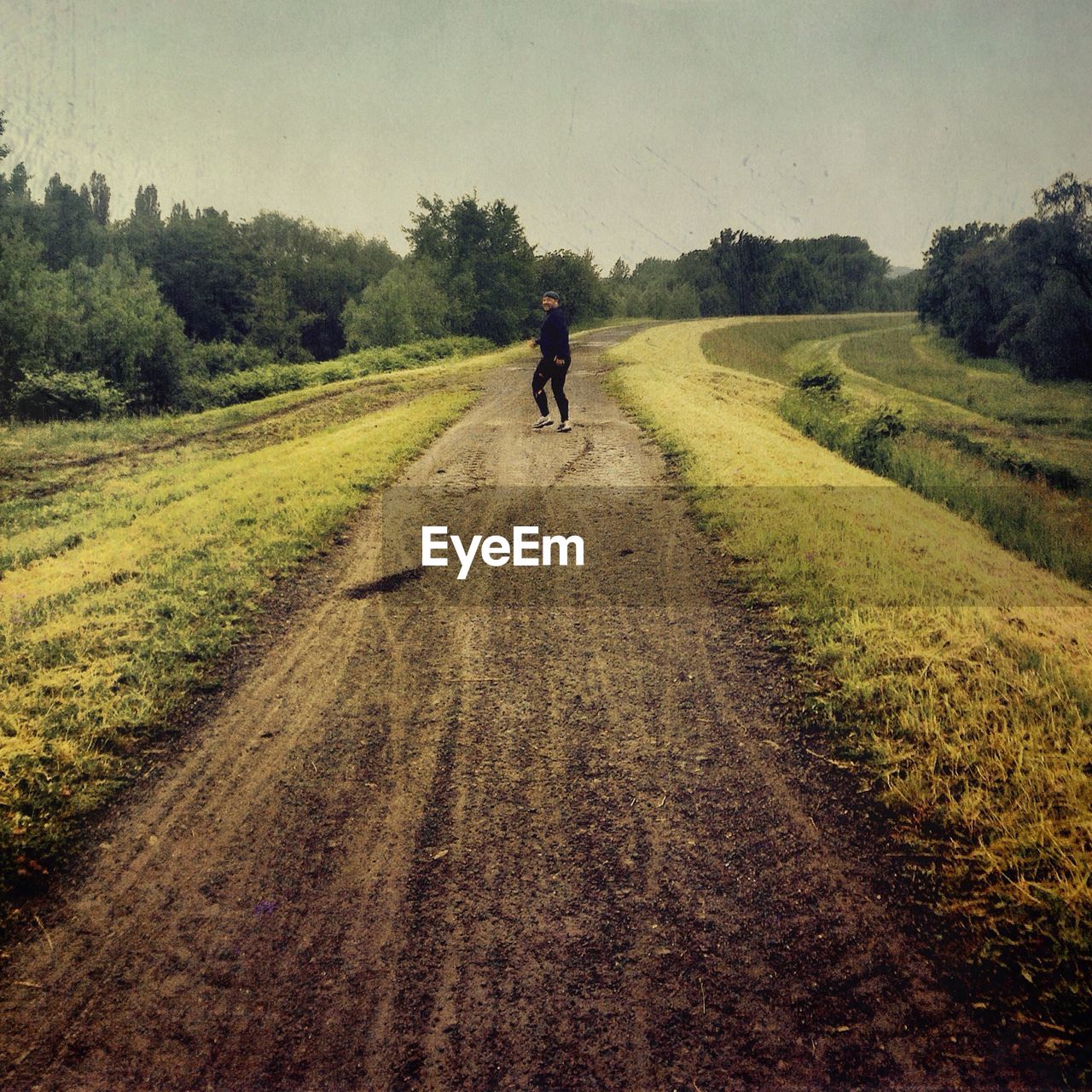 Man walking on dirt road amidst field against sky