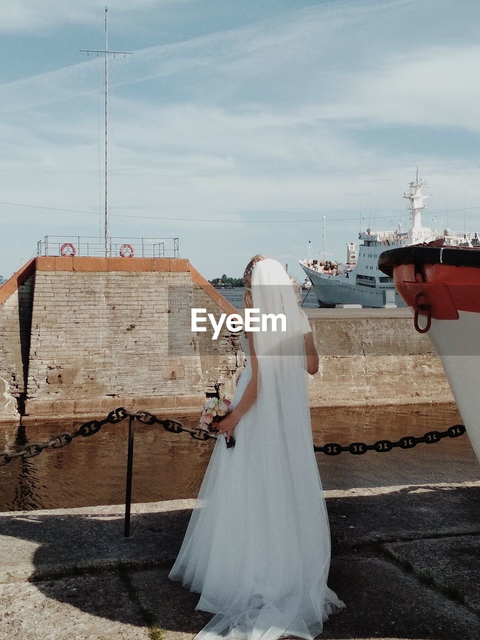 Rear view of bride standing at port against sky