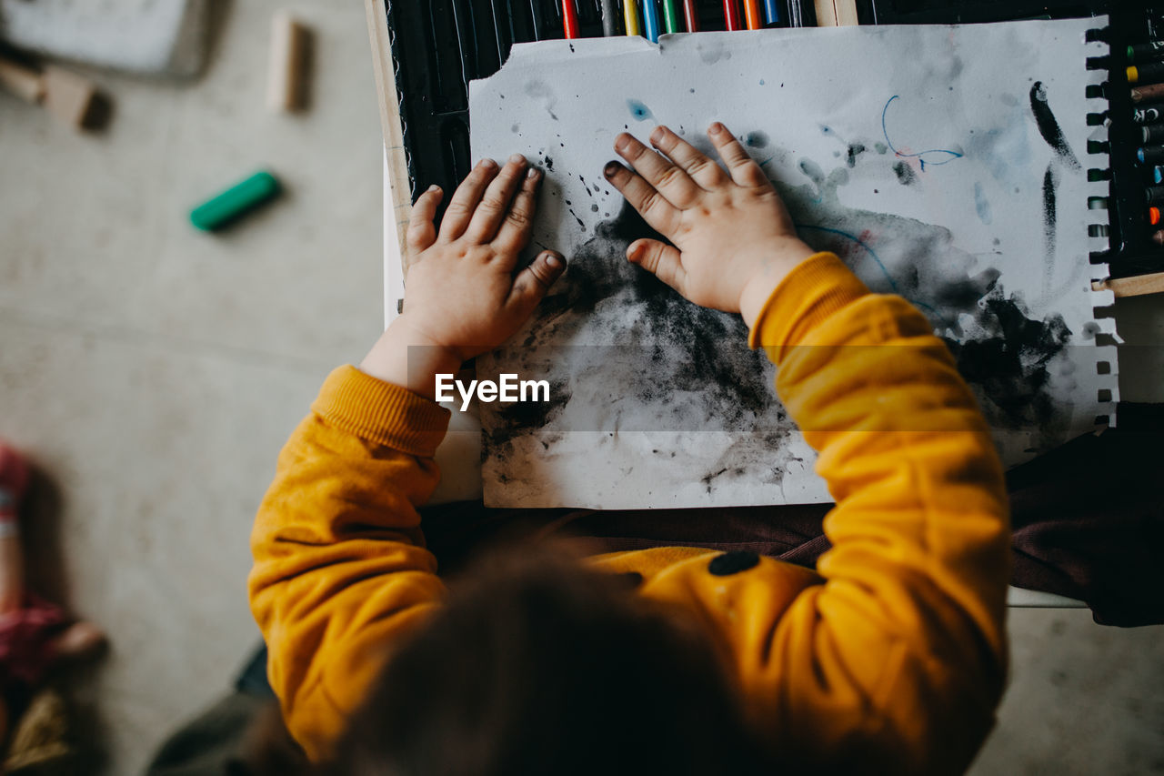 High angle view of child painting with hands on floor