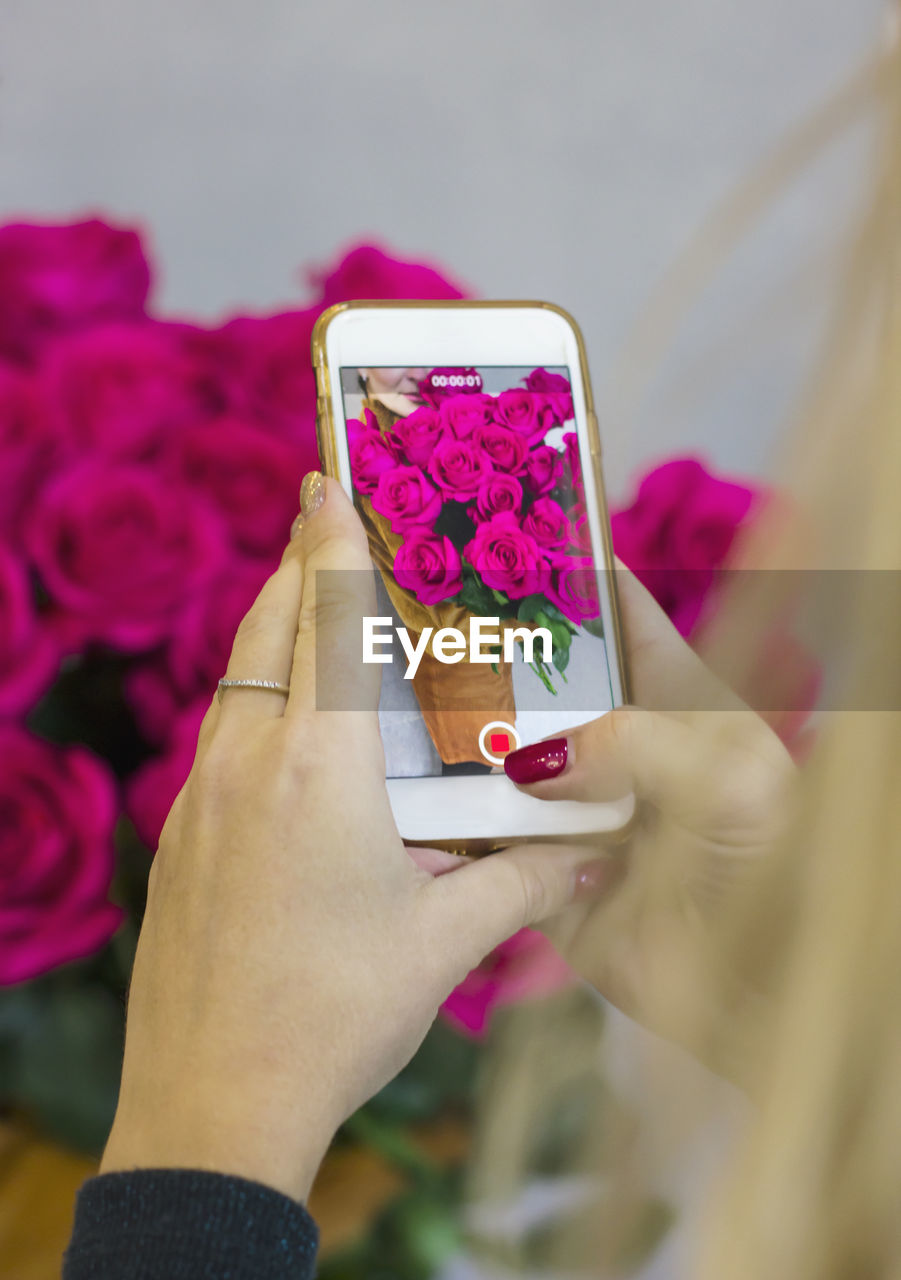 Cropped hand of woman photographing flower bouquet with mobile phone