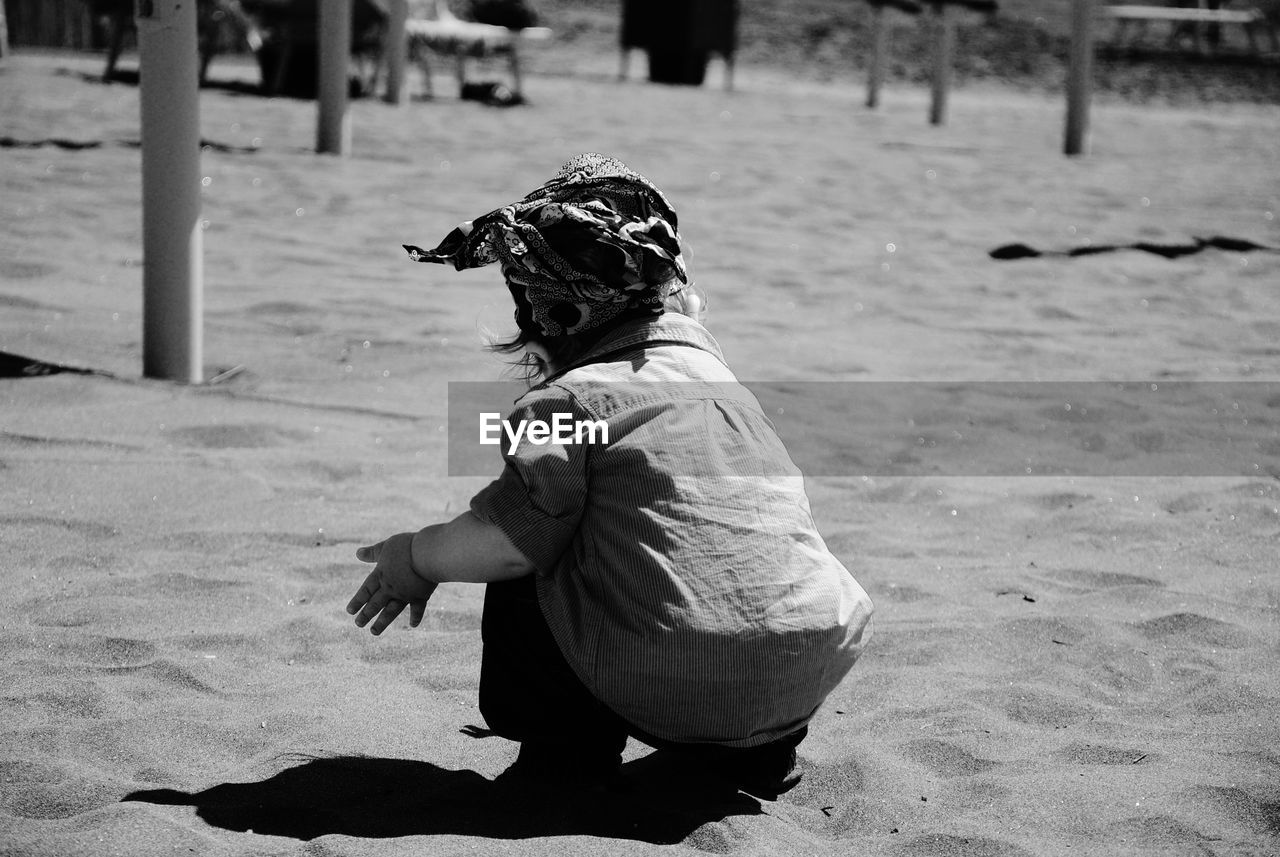 Rear view of baby girl crouching on sand at beach during sunny day