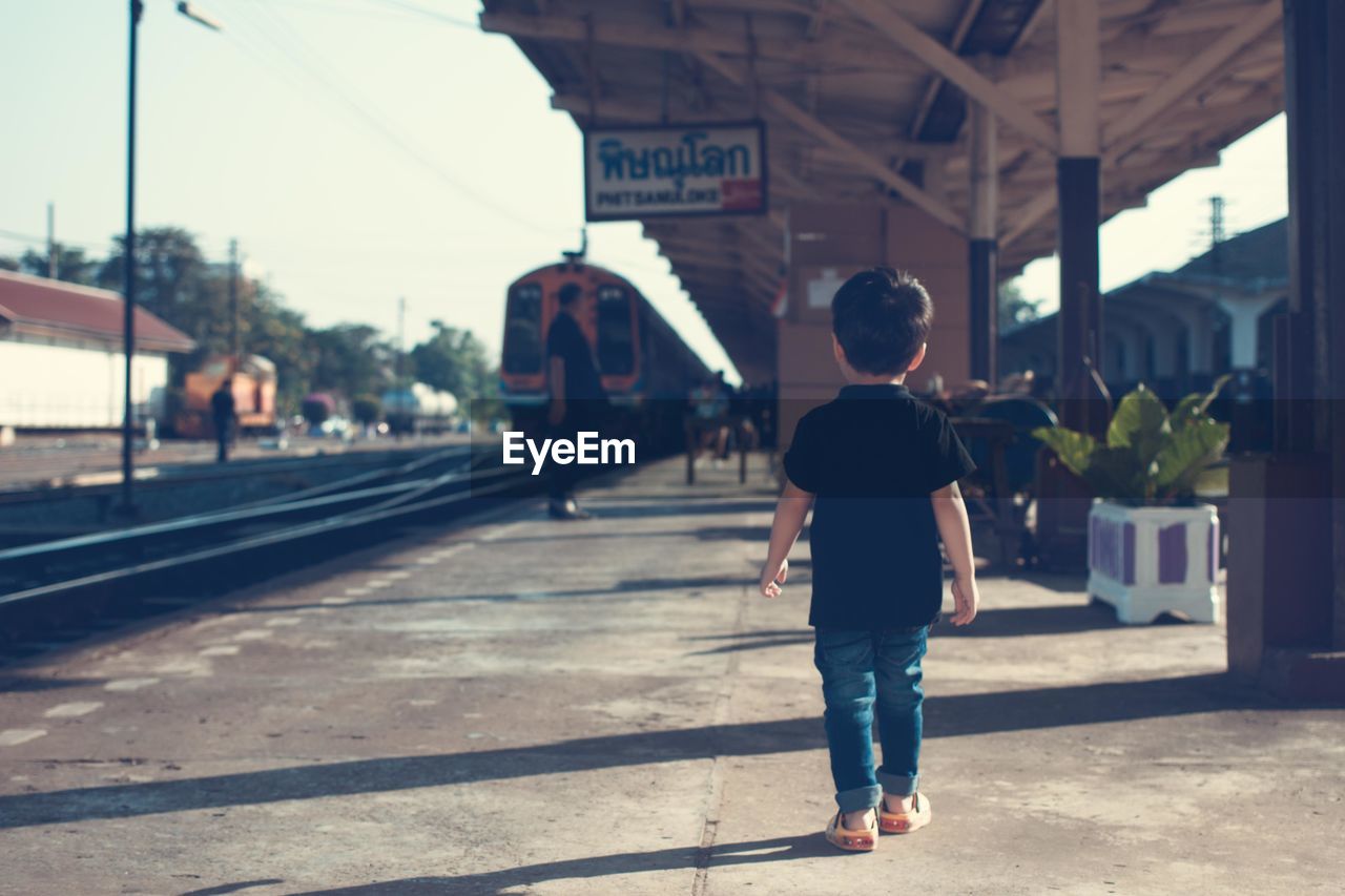 Full length rear view of boy walking at railroad station platform