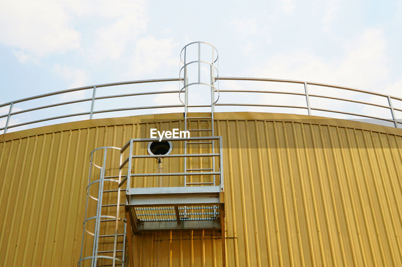 Low angle view of yellow cylindrical tank against sky