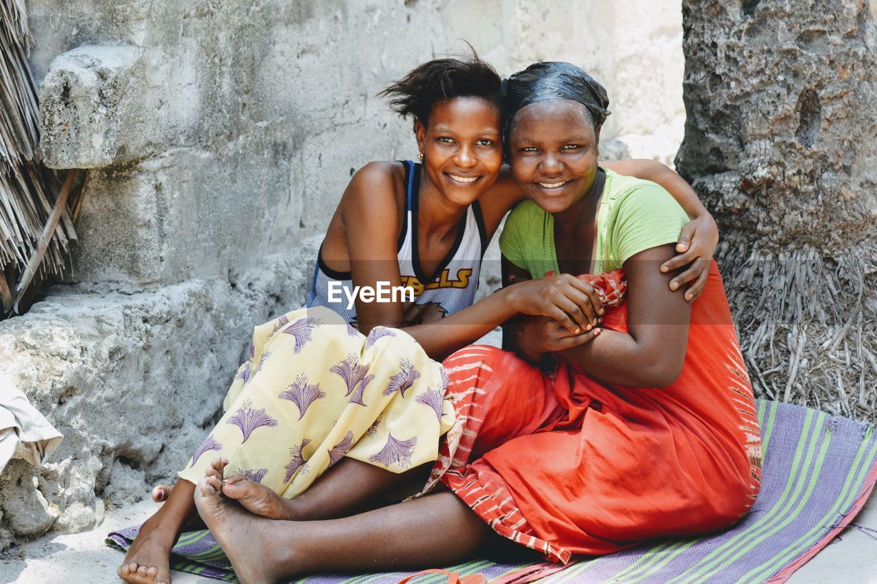 Portrait of female friends smiling while sitting against wall