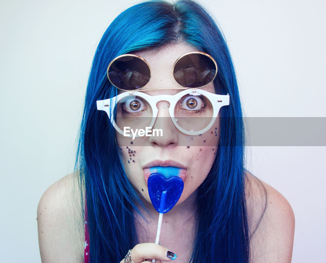 Portrait of woman wearing sunglasses while eating candy against wall