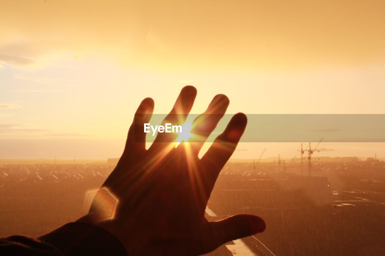 Cropped hand of man against sun during sunset
