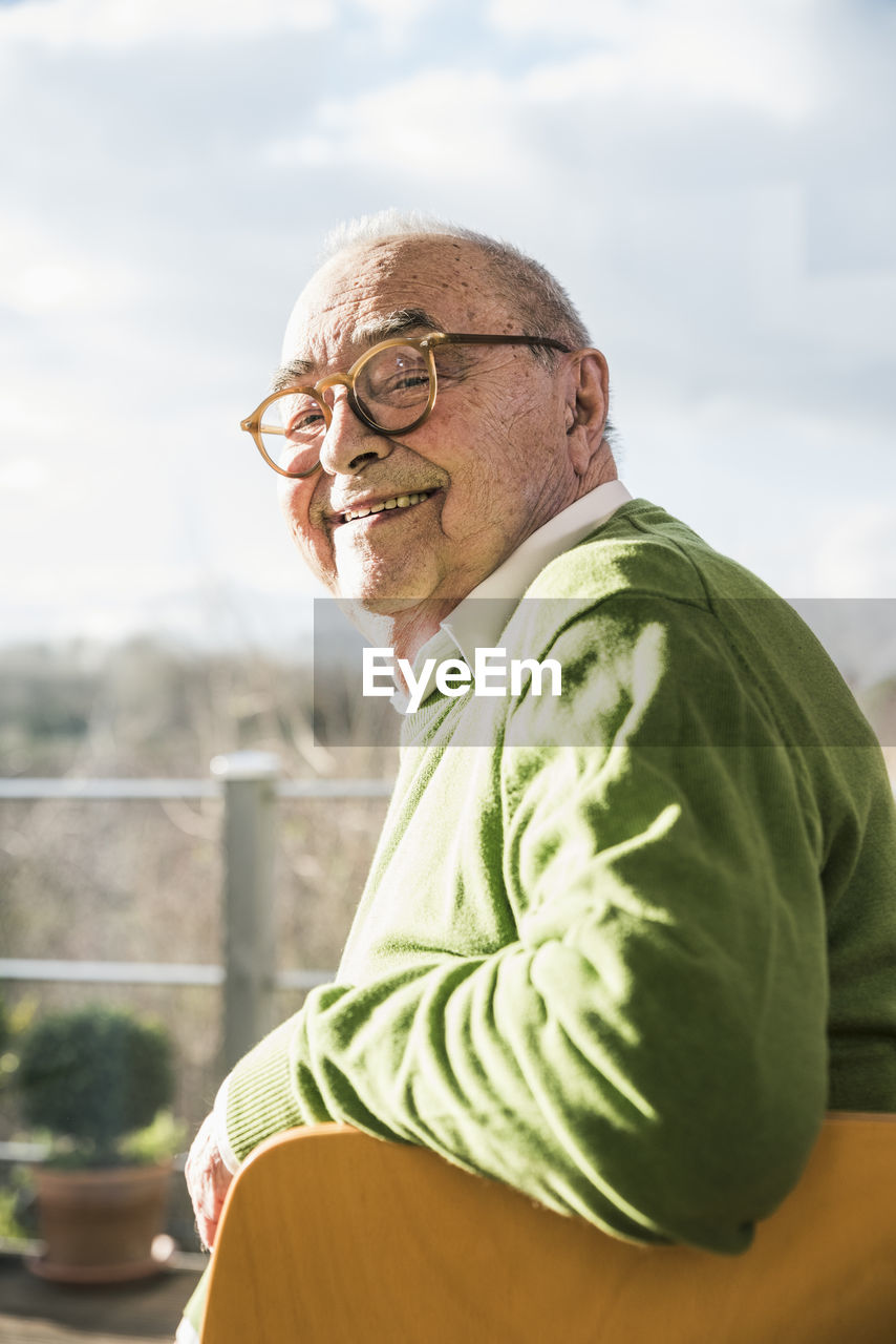 Portrait of smiling senior man sitting on chair at the window