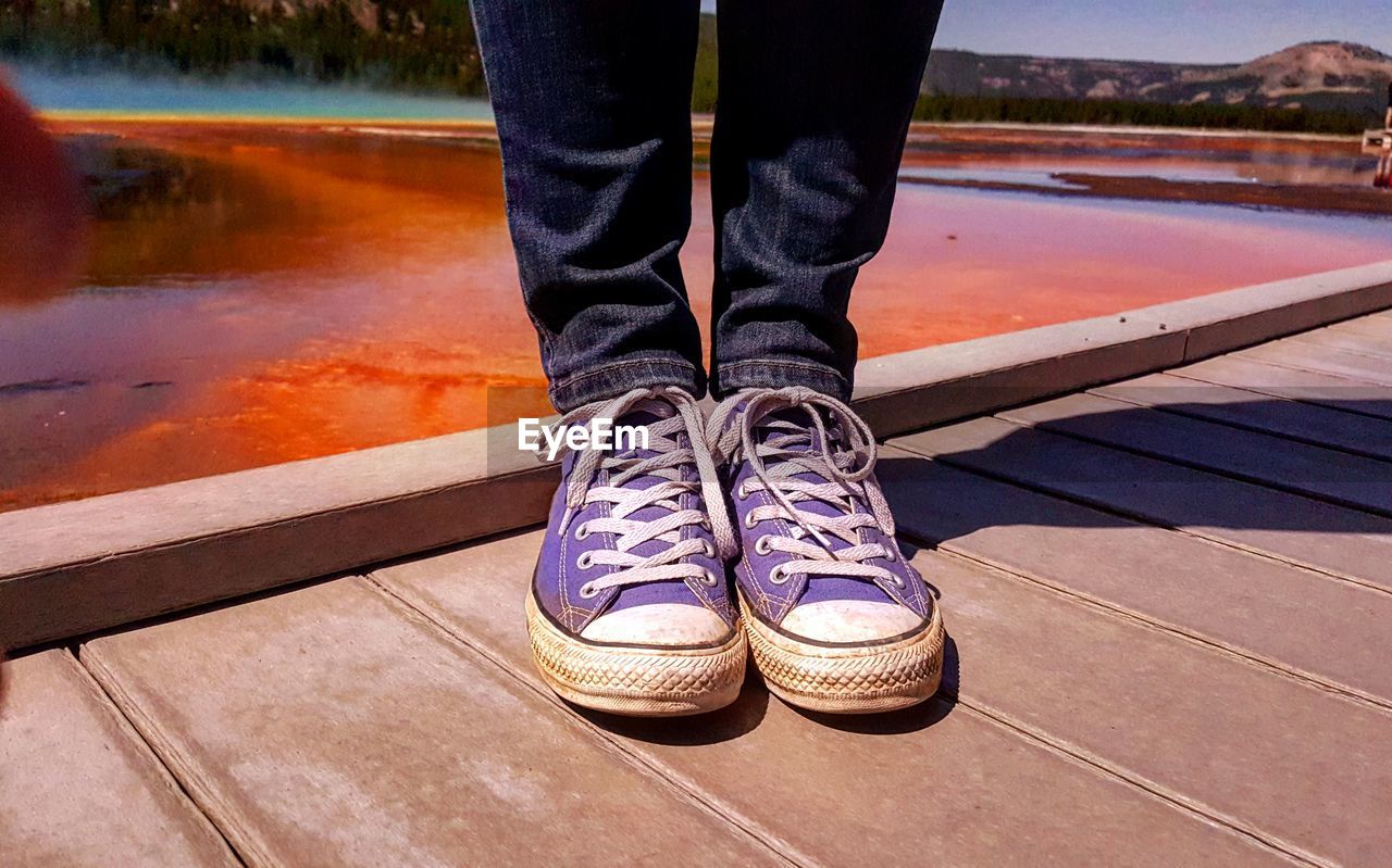 Low section of man standing on boardwalk over geyser