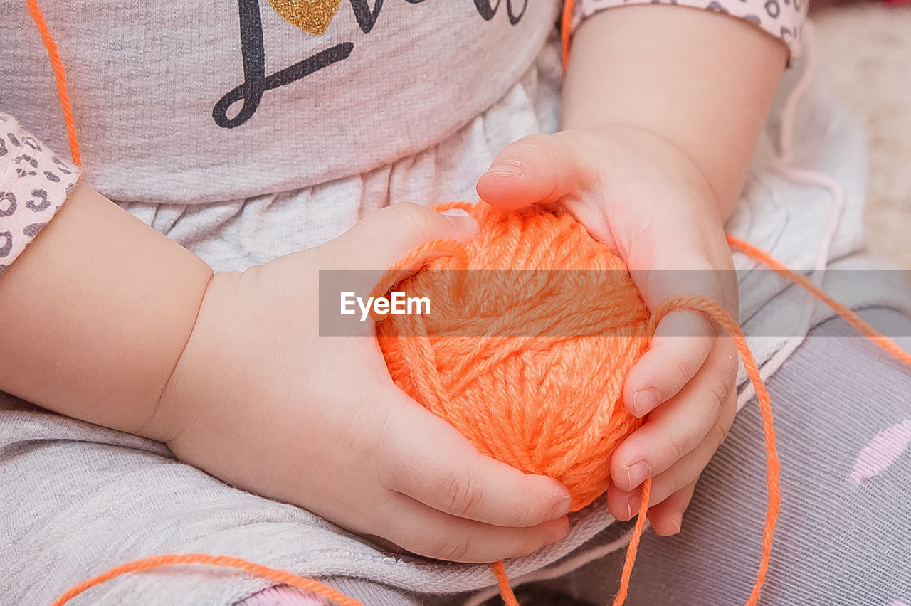 A small child is holding a ball of thread in his hands. the yarn is in the girl's palms