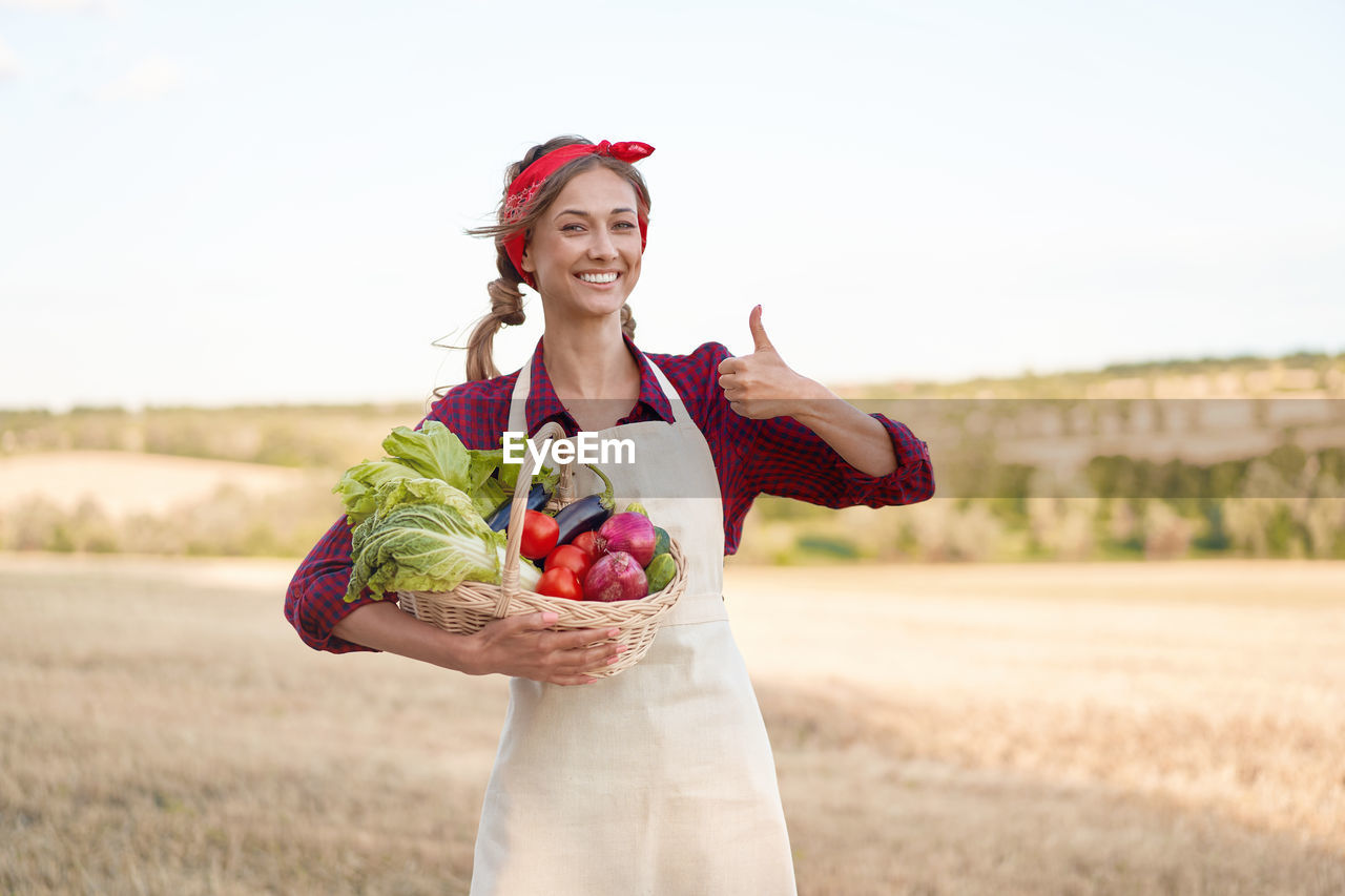 YOUNG WOMAN SMILING WHILE STANDING IN FIELD