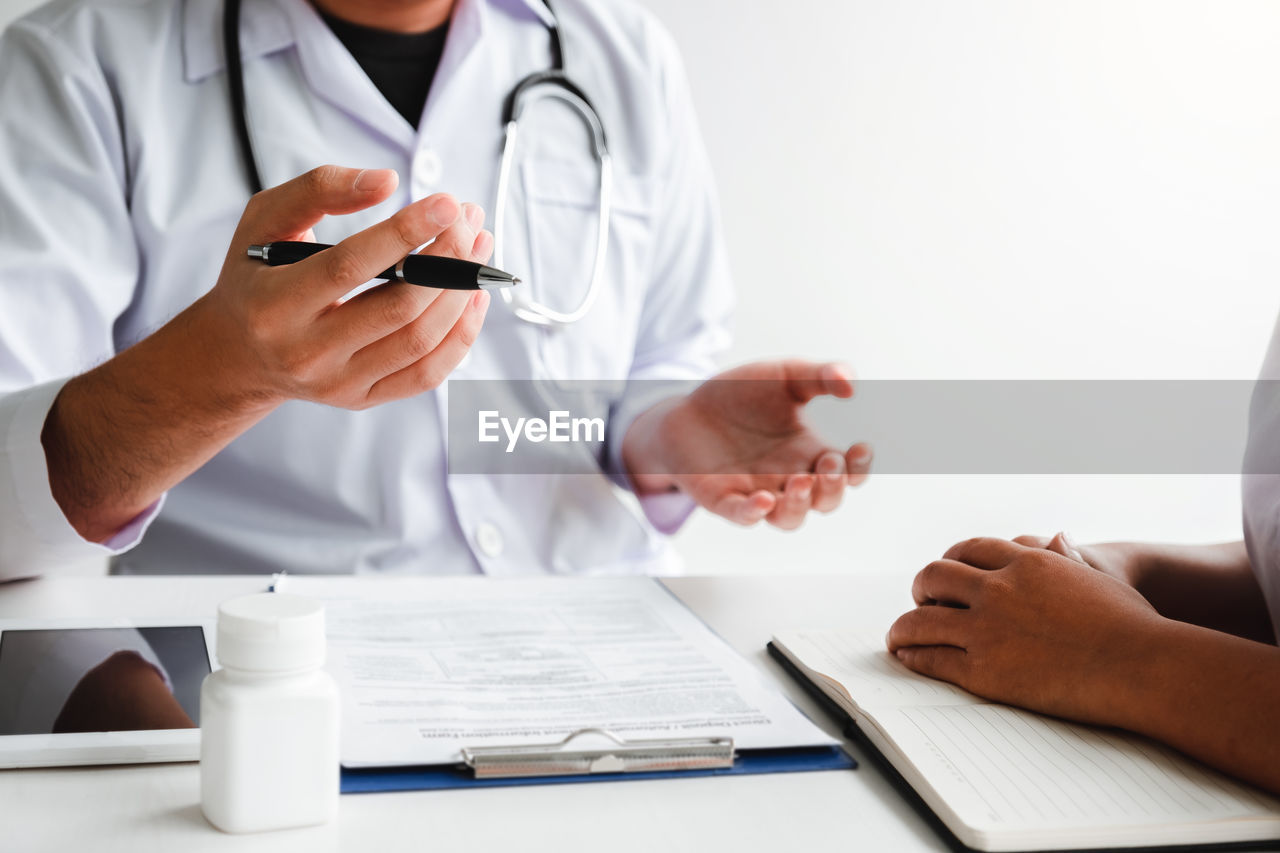 midsection of doctor using mobile phone while sitting at clinic