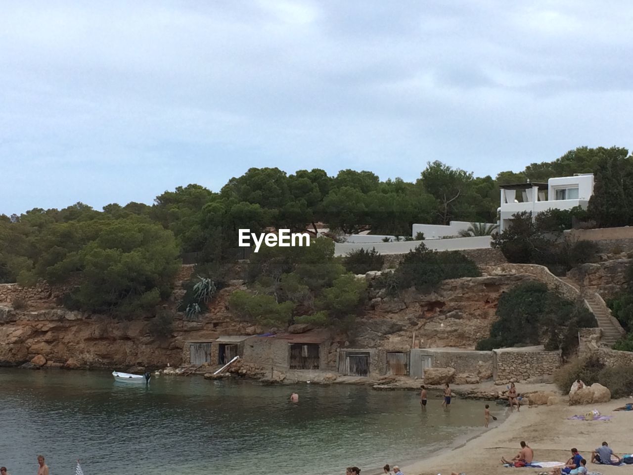 People at cala gracio beach against cloudy sky