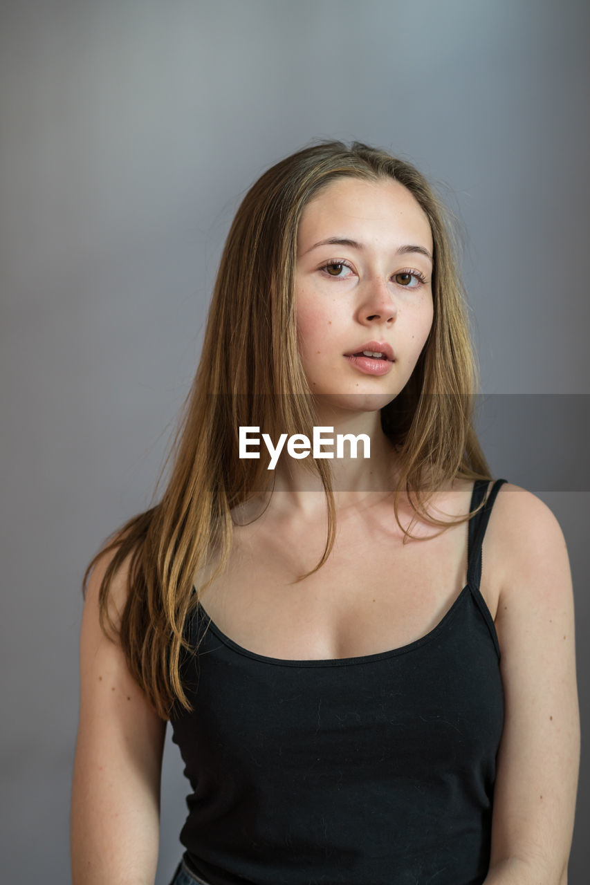 Portrait of a charming young woman wearing a camisole posing looking at camera on grey background