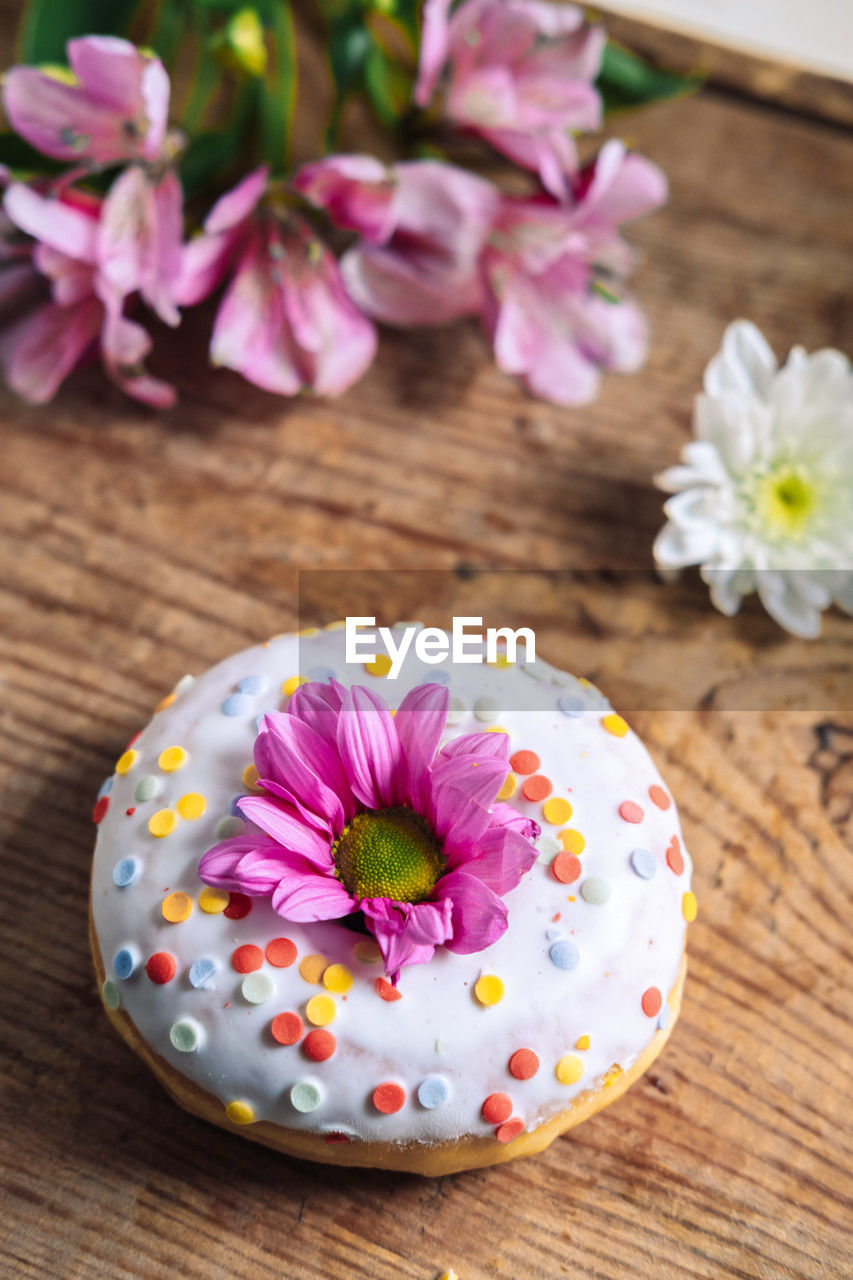 Chamomile bud on top of a donut on a wooden background with a bouquet of alstroemerias. 	