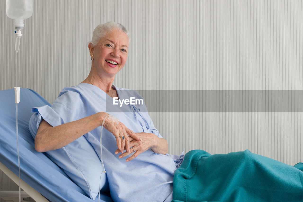 Portrait of smiling senior woman sitting on bed in hospital