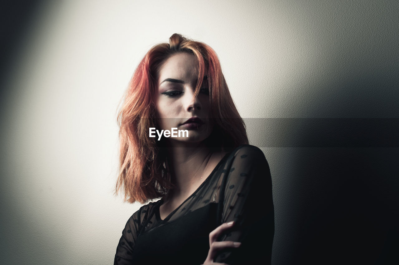 Beautiful young woman looking away while standing against wall