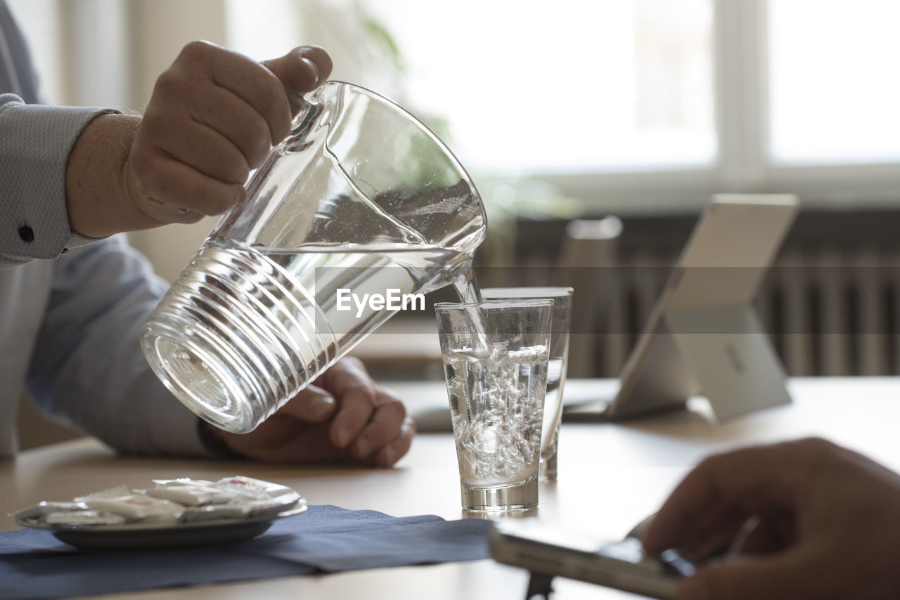 midsection of man holding coffee in glass on table