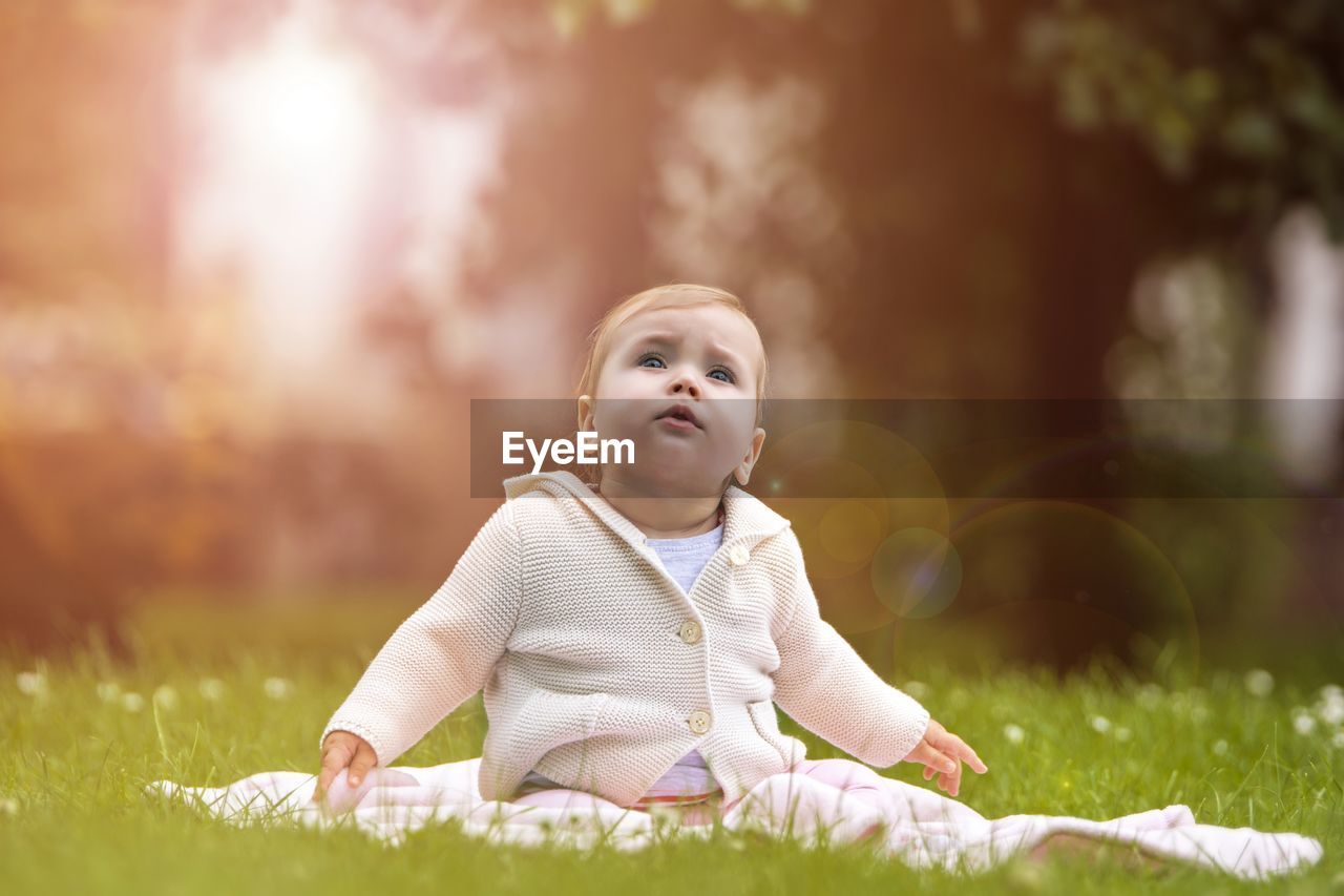 Full length of cute baby girl looking up sitting on grassy field 
