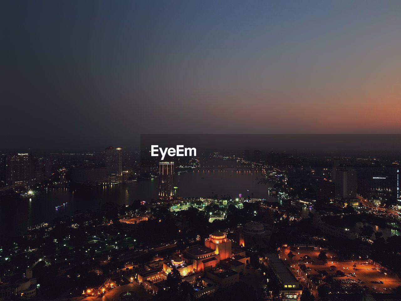 HIGH ANGLE VIEW OF ILLUMINATED BUILDINGS IN CITY AGAINST SKY