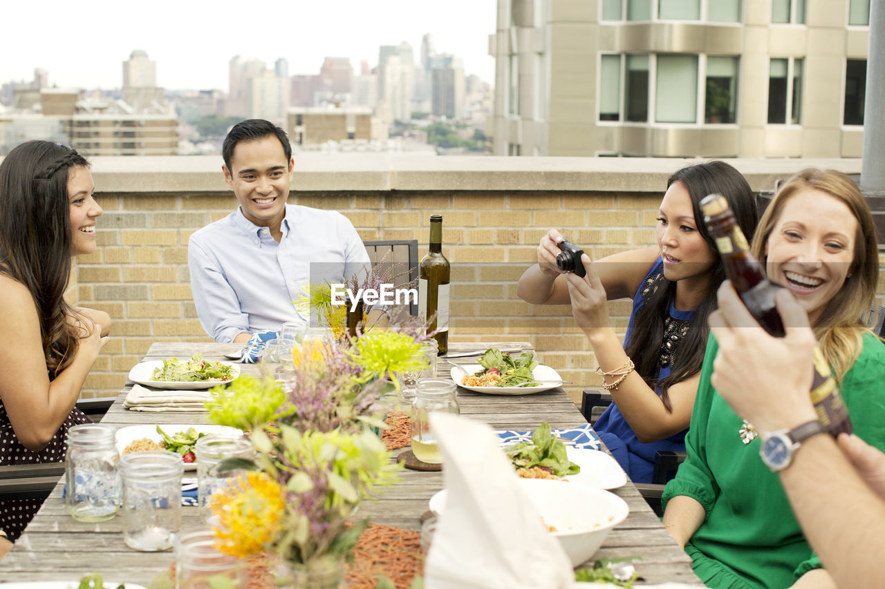 Happy friends enjoying meal on building terrace in city