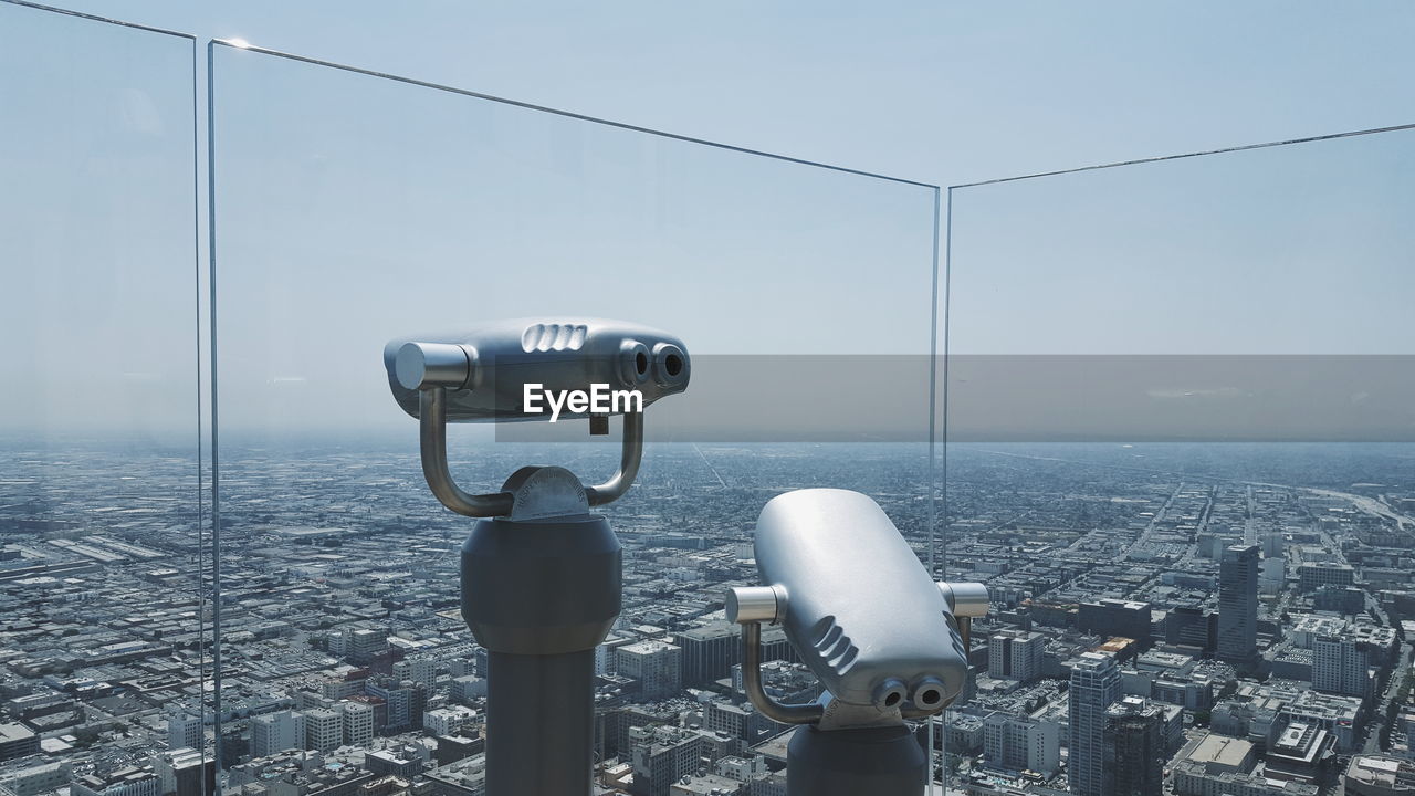 Coin-operated binoculars by glass against cityscape