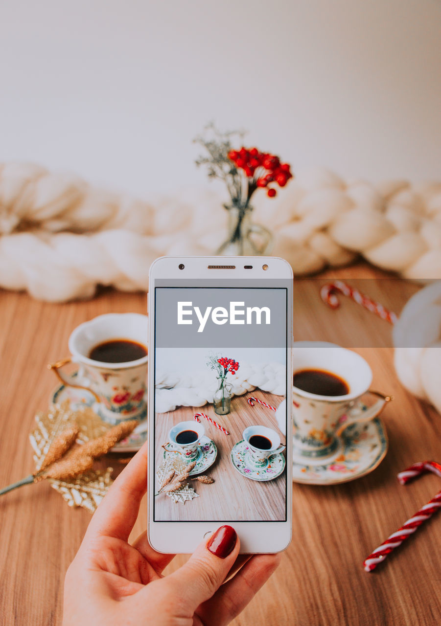 Close-up of hand photographing coffee cups on mobile phone at table