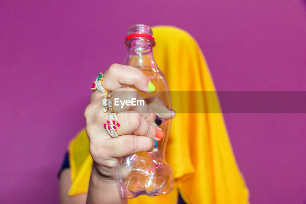 Midsection of woman holding glass bottle against pink background