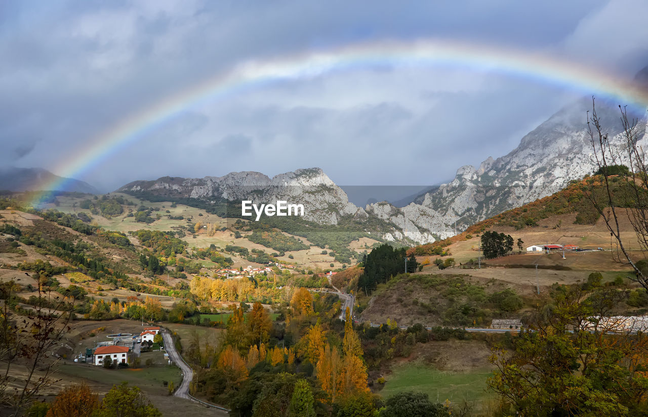 Picturesque autumn landscape of high mountains with low clouds, rainbow and green trees in cantabria