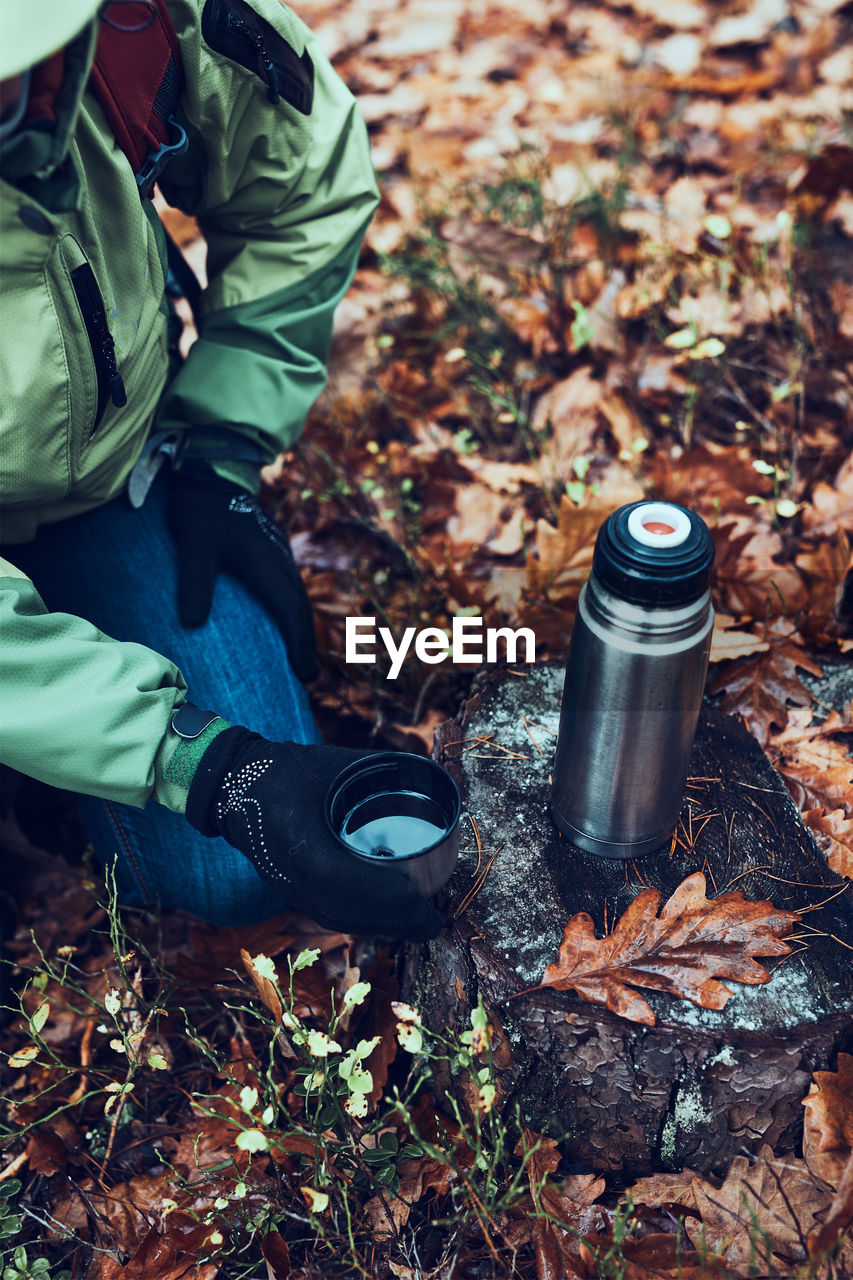 Woman with backpack having break during trip on autumn cold day drinking a hot drink from thermos