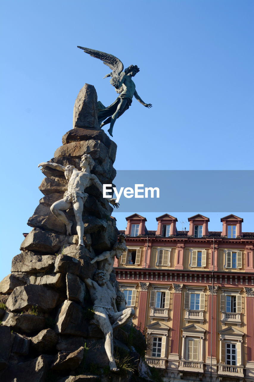 Low angle view of statue against building against clear blue sky