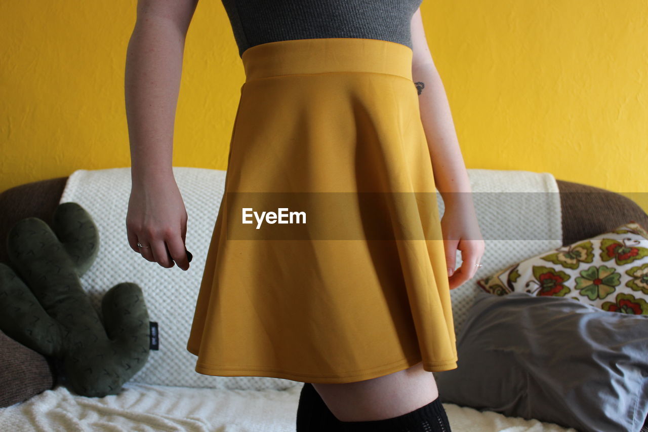 Midsection of woman wearing yellow skirt against sofa at home
