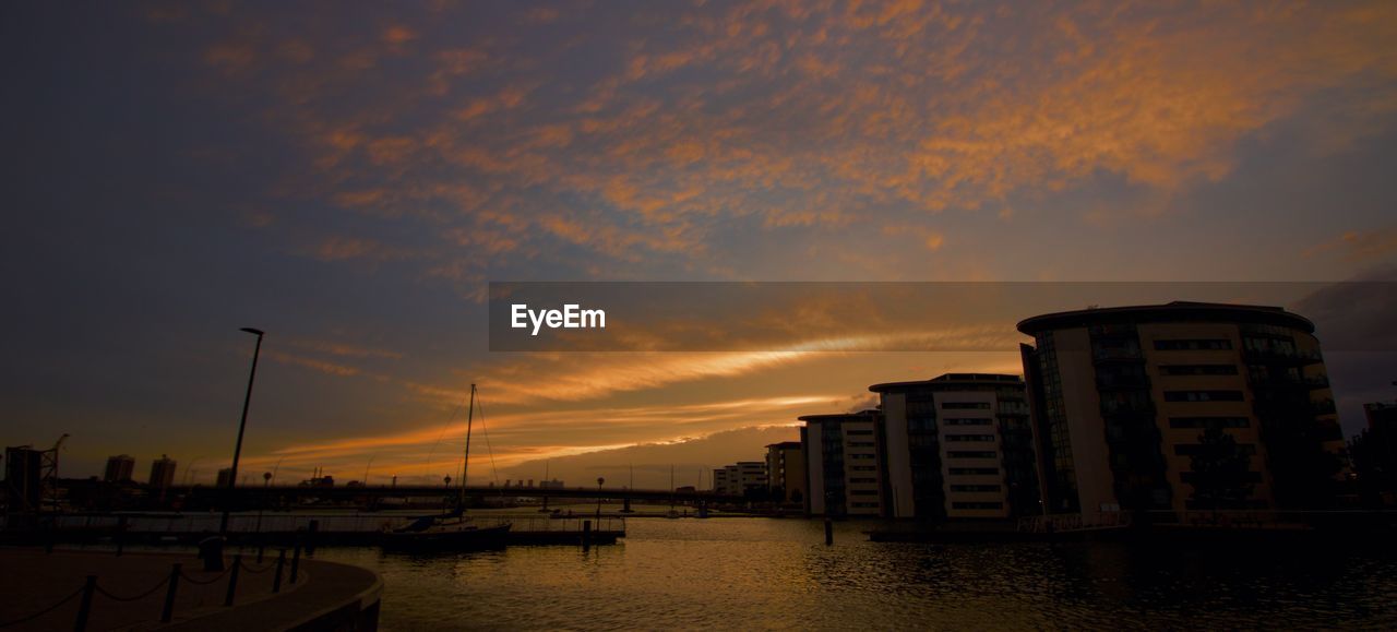 BUILDINGS BY SEA AGAINST ORANGE SKY