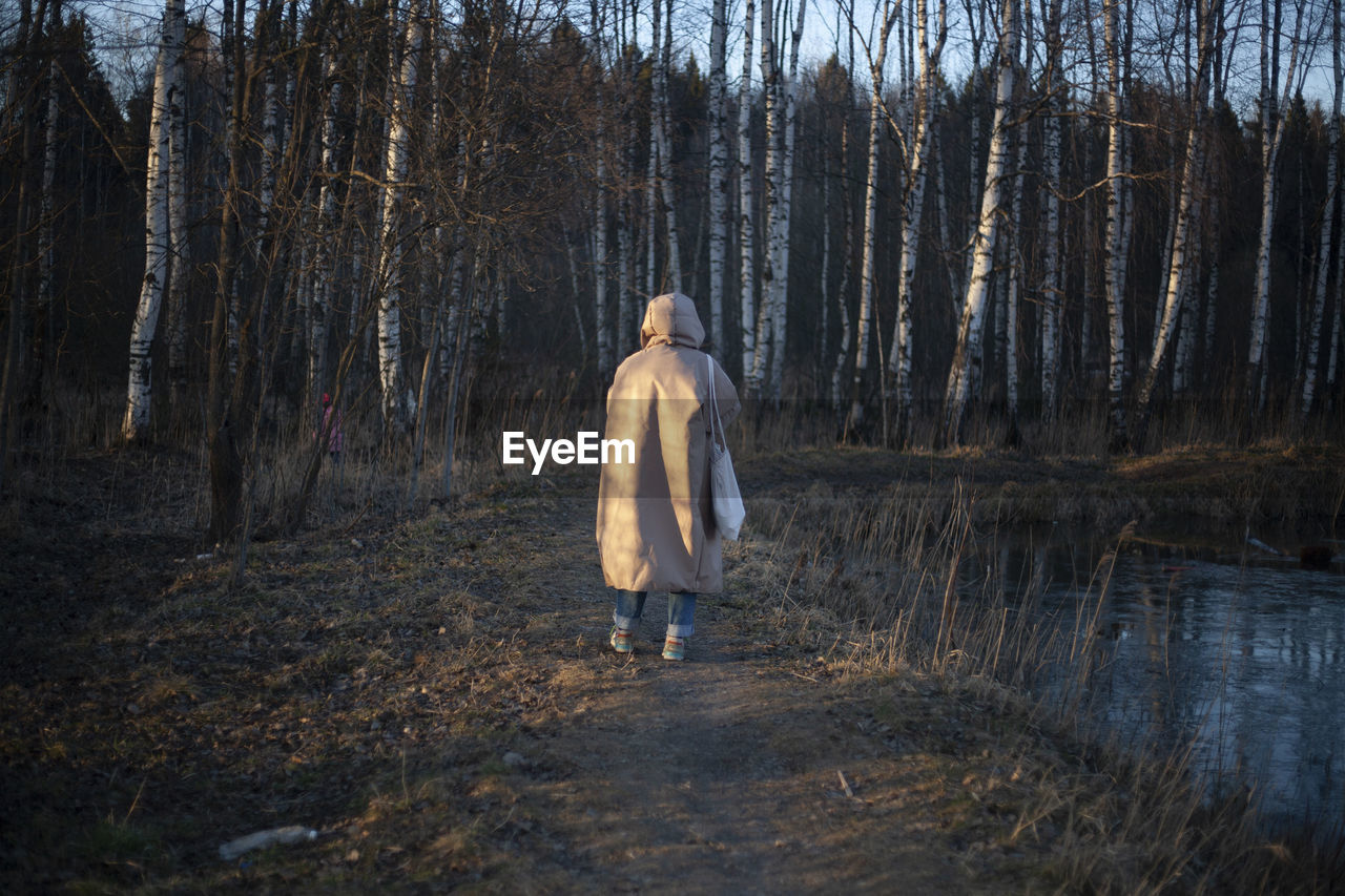 Rear view of man walking by lake in forest