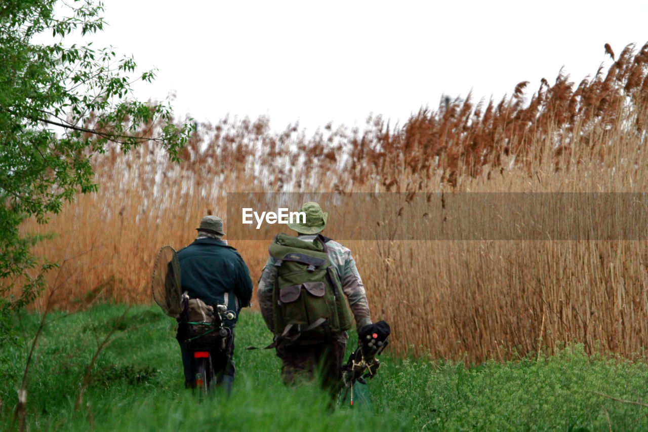 Rear view of friends walking on field against sky