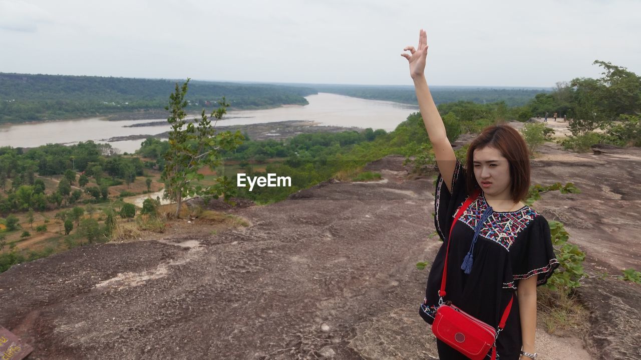 Young woman standing with hand raised on mountain