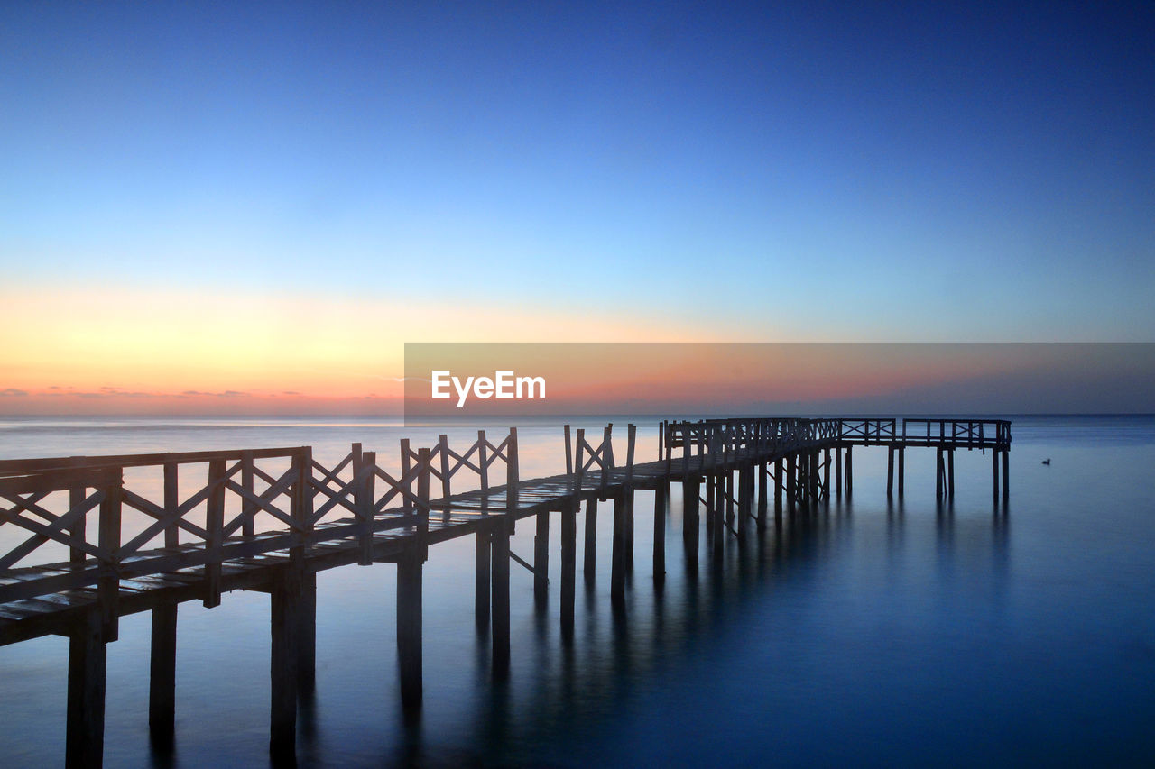 Pier over sea against clear sky during sunset