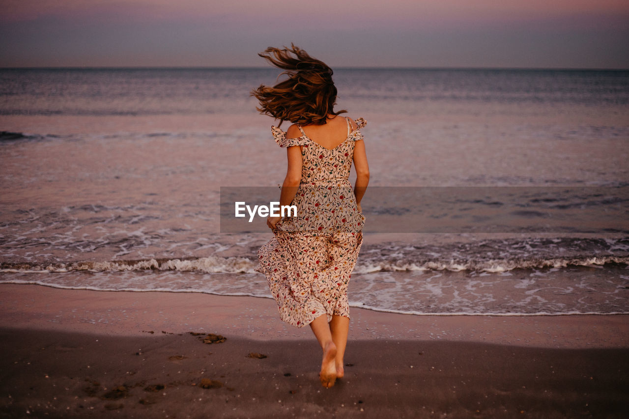 Rear view of woman standing at beach during sunset