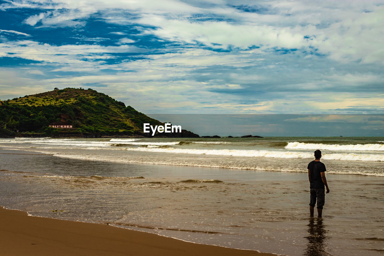 FULL LENGTH REAR VIEW OF MAN ON BEACH AGAINST SKY