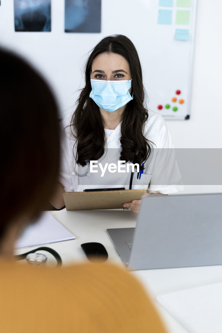 Female doctor talking with patient at clinic during pandemic