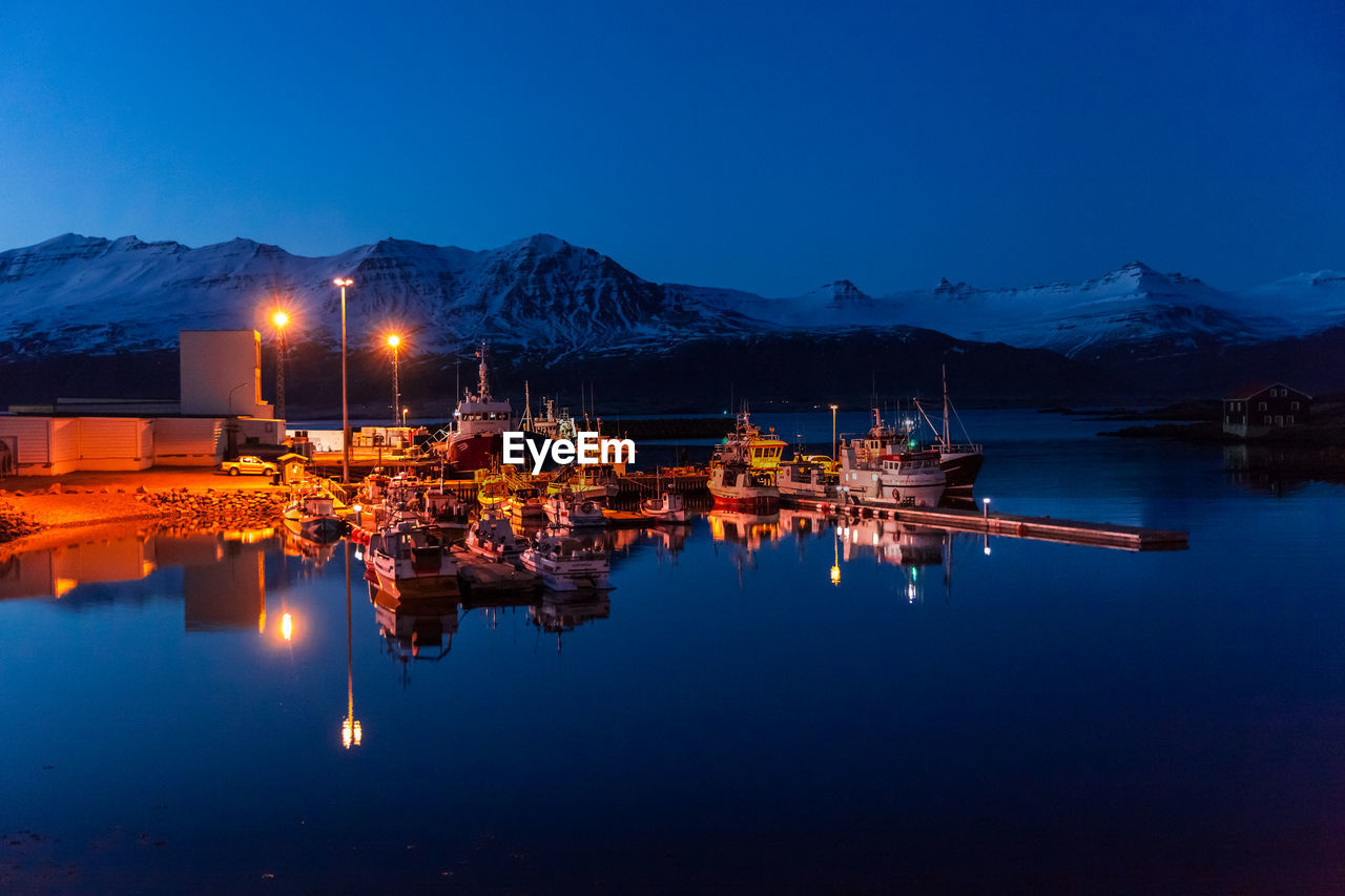 Illuminated harbor against snowcapped mountain at night