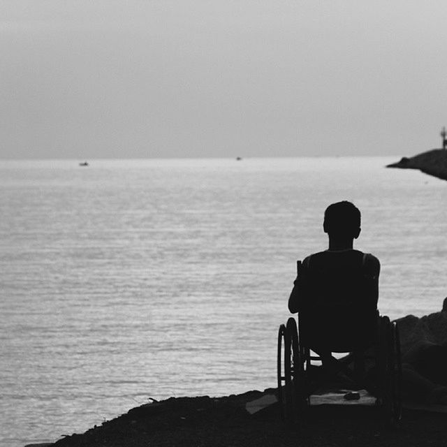 Silhouette of person in wheelchair looking at sea