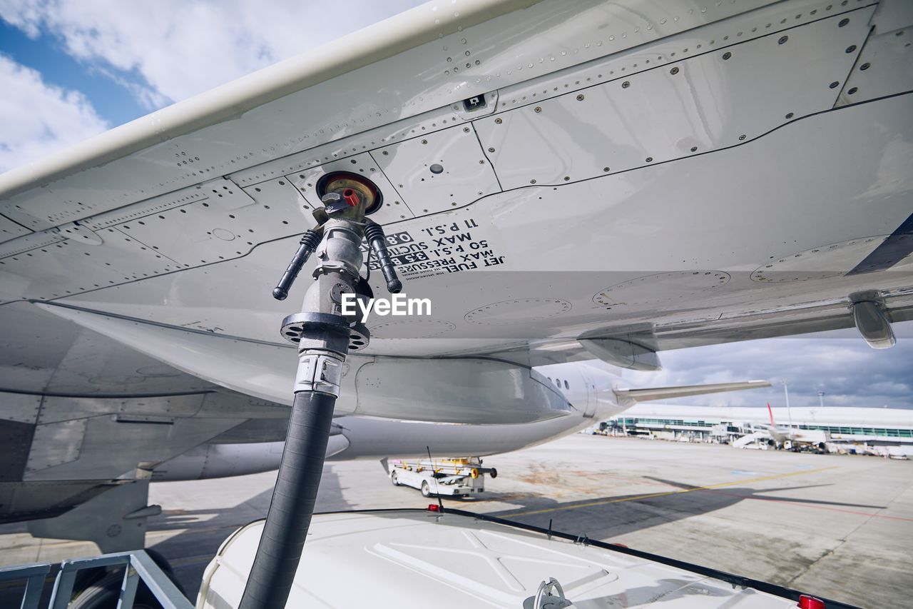 Airplane refueling at airport runway against sky