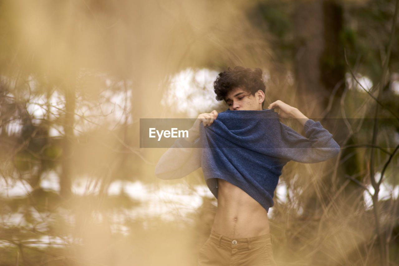 Young man wearing sweater while standing at forest