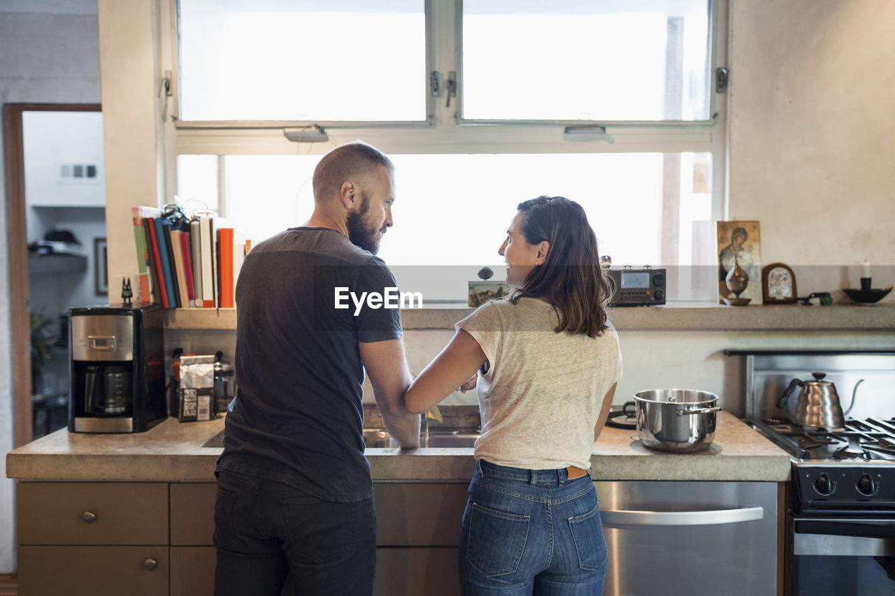 Rear view of couple looking at each other in kitchen